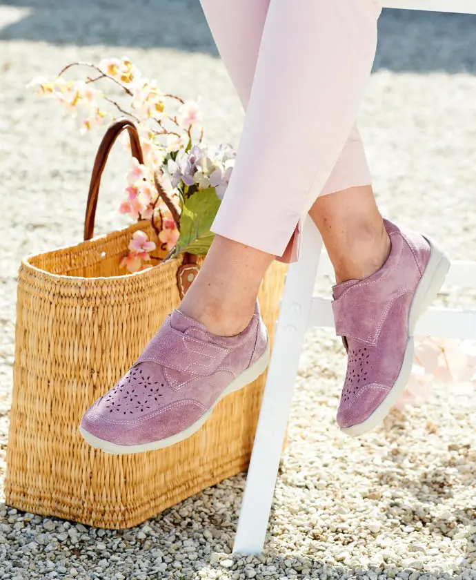 A woman sat wearing a pair of pink shoes with a rattan bag