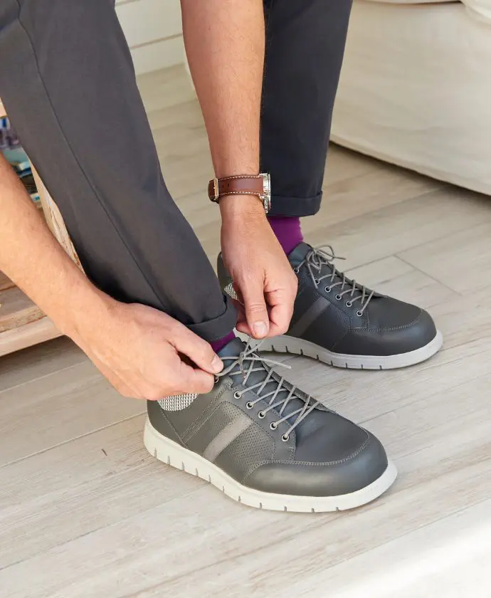 Someone bent down tying up shoelaces on grey shoes