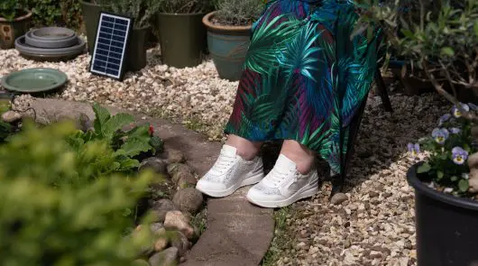 Someone sat in a garden with a green dress and white trainers