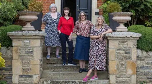 4 women standing together on steps of a grand looking house